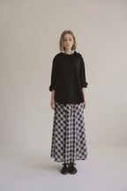 模特兒穿著黑色格紋斜裁綁帶長裙，腰間綁帶與腰釦修飾比例，兩側口袋與裙擺歐干紗營造修長優雅造型。