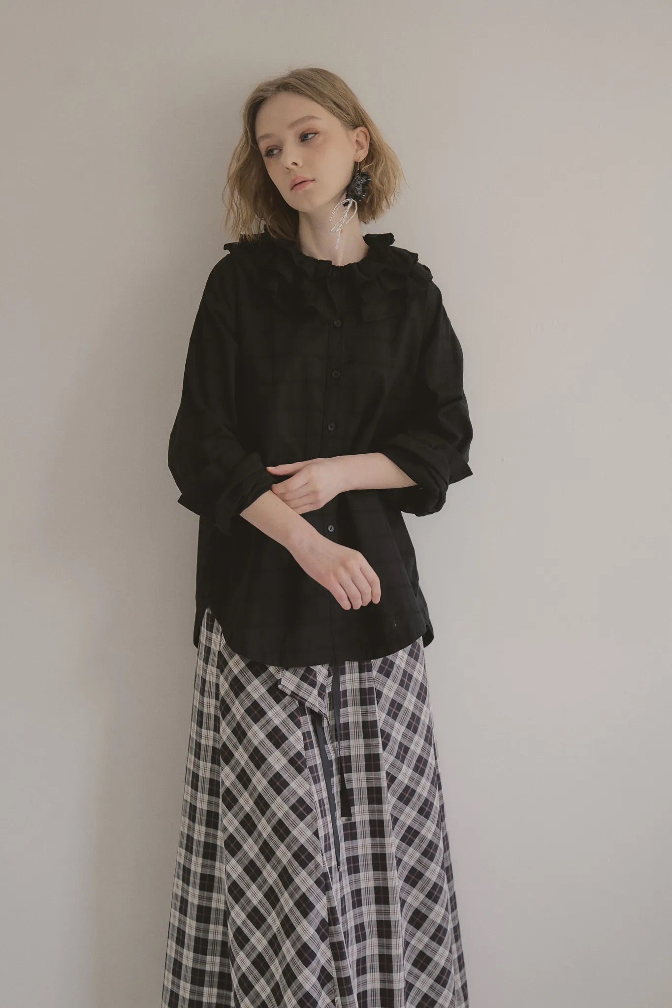 模特兒穿著黑色格紋斜裁綁帶長裙，腰間綁帶與腰釦修飾比例，兩側口袋與裙擺歐干紗營造修長優雅造型。