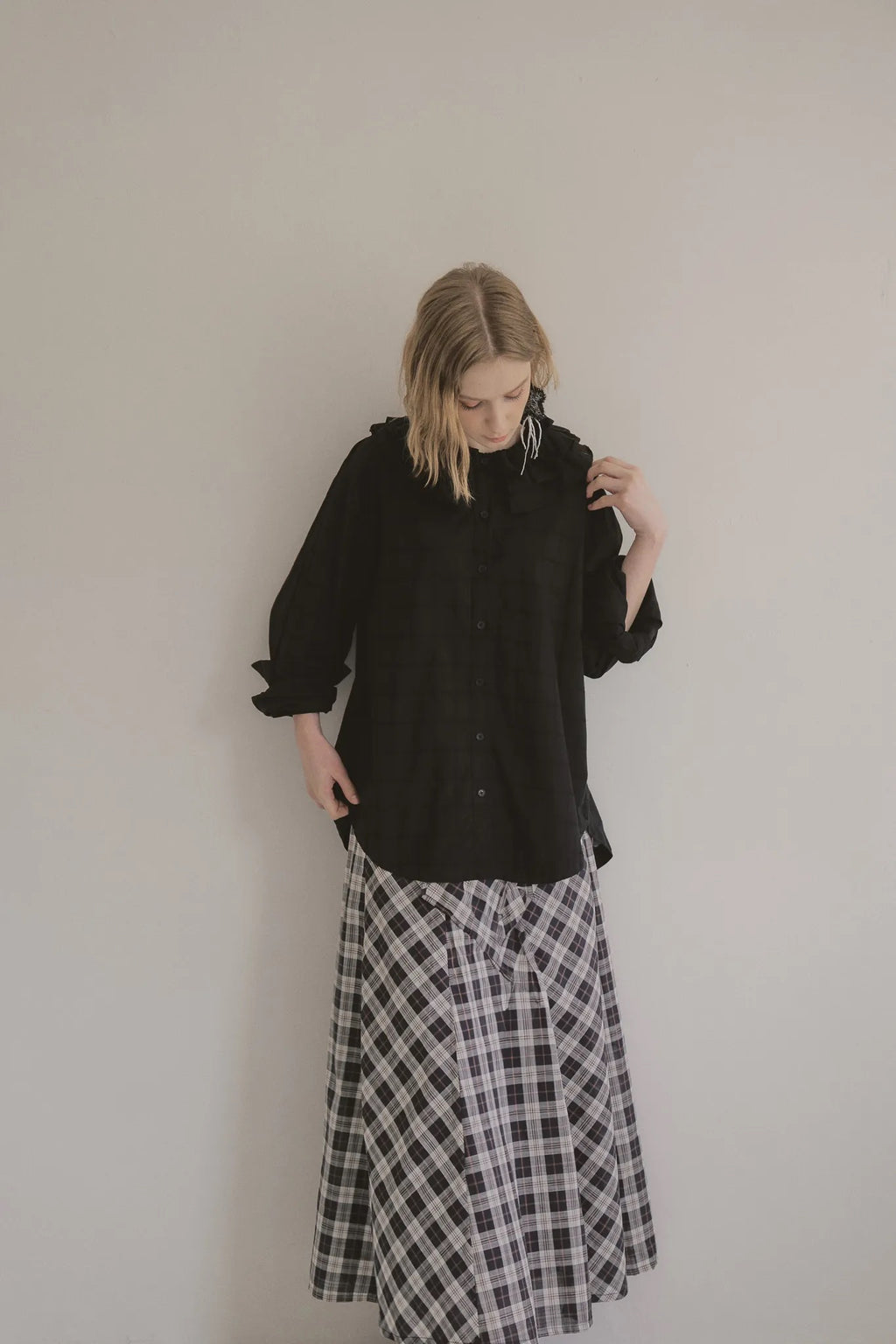 模特兒穿著黑色格紋斜裁綁帶長裙，腰間綁帶與腰釦修飾比例，兩側口袋與裙擺歐干紗營造修長優雅造型。