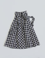 模特兒穿著黑色格紋斜裁綁帶長裙，腰間綁帶與腰釦修飾比例，兩側口袋與裙擺歐干紗營造修長優雅造型。