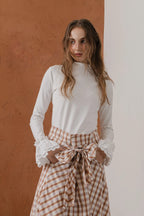 模特兒穿著紅棕色格紋斜裁綁帶長裙，腰間綁帶與腰釦修飾比例，兩側口袋與裙擺歐干紗營造修長優雅造型。