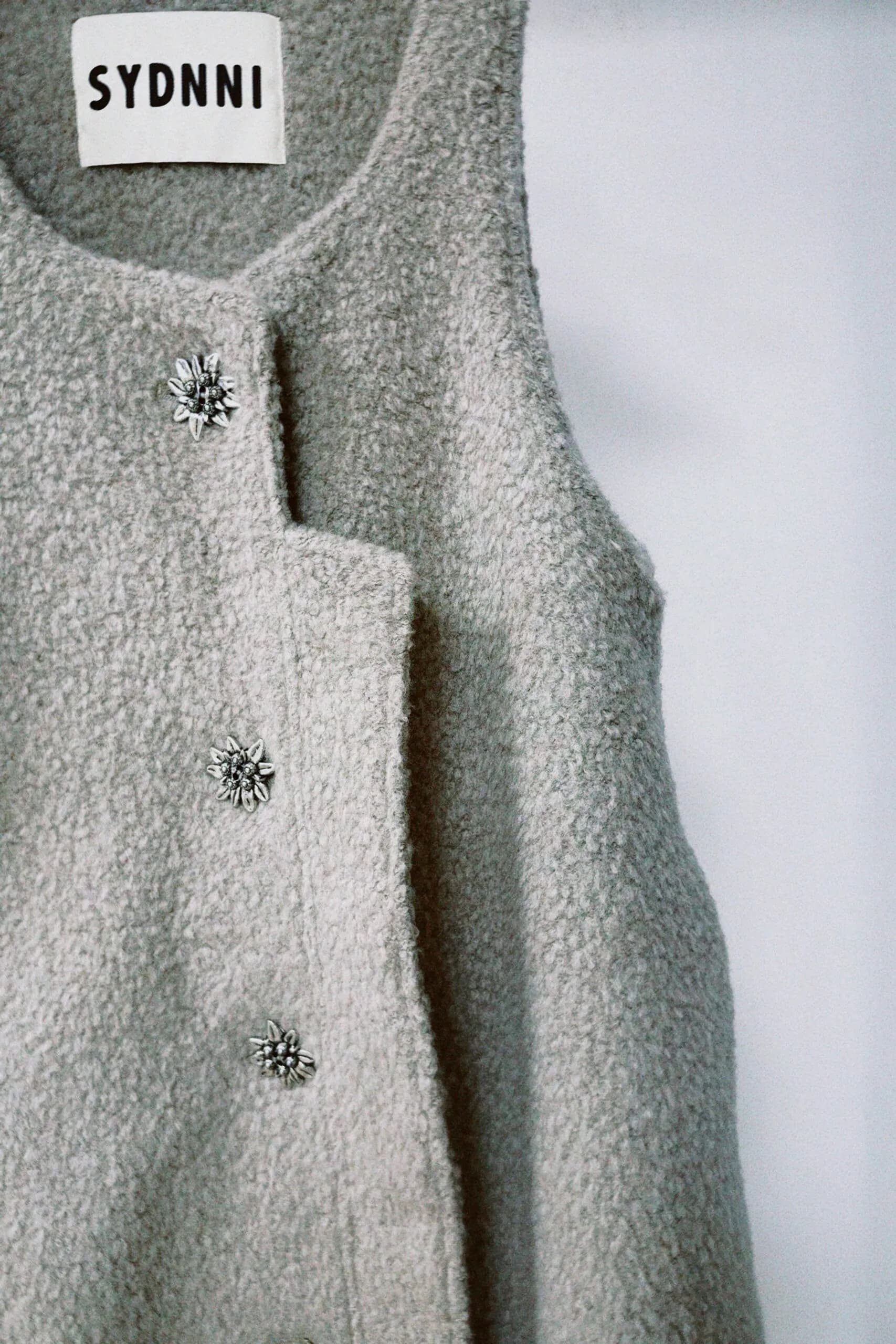 朦朧灰羊絨背心洋裝外套近照，柔軟羊絨面料搭配立體花釦、後開衩與側袋設計，展現優雅多變造型。