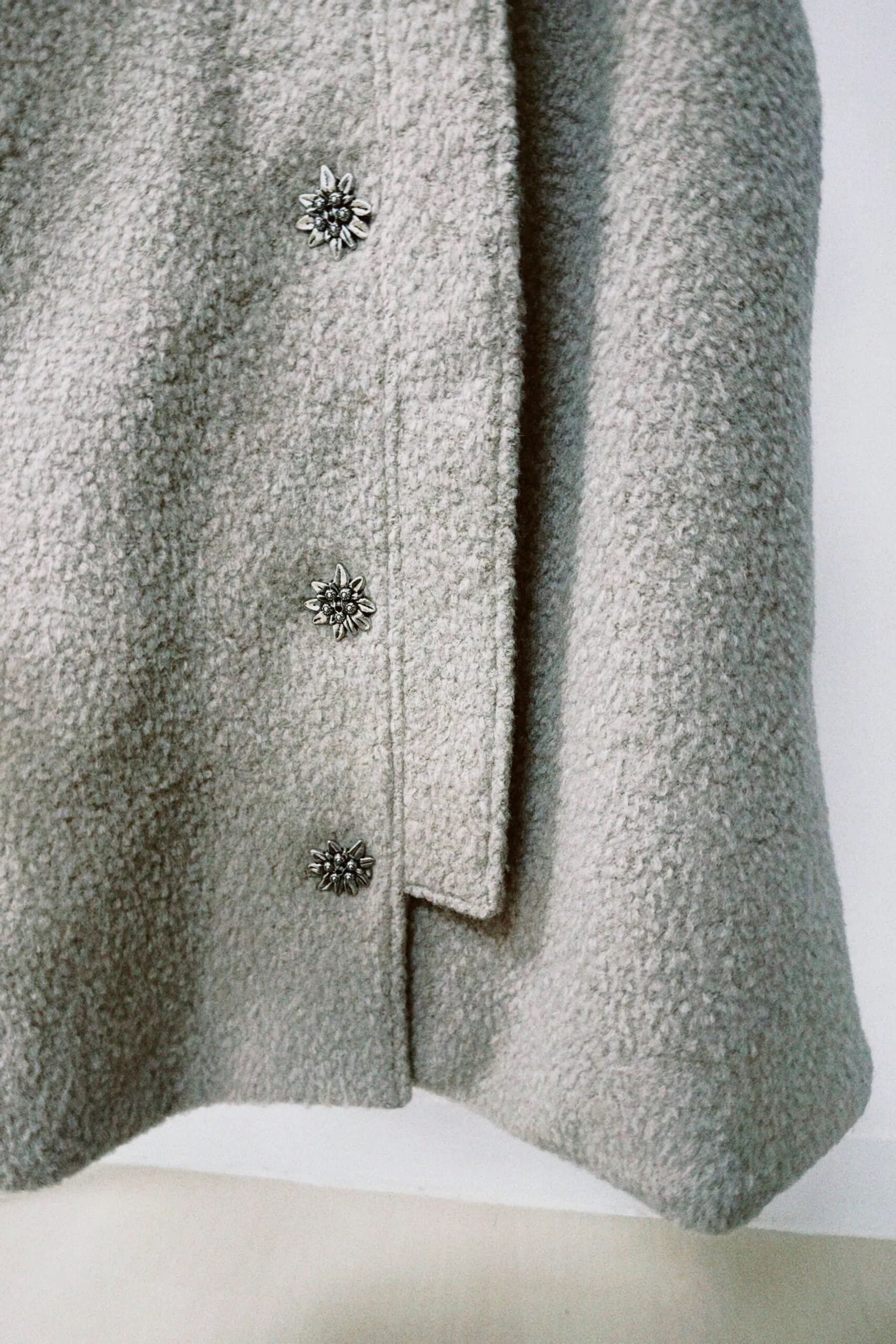 朦朧灰羊絨背心洋裝外套近照，柔軟羊絨面料搭配立體花釦、後開衩與側袋設計，展現優雅多變造型。