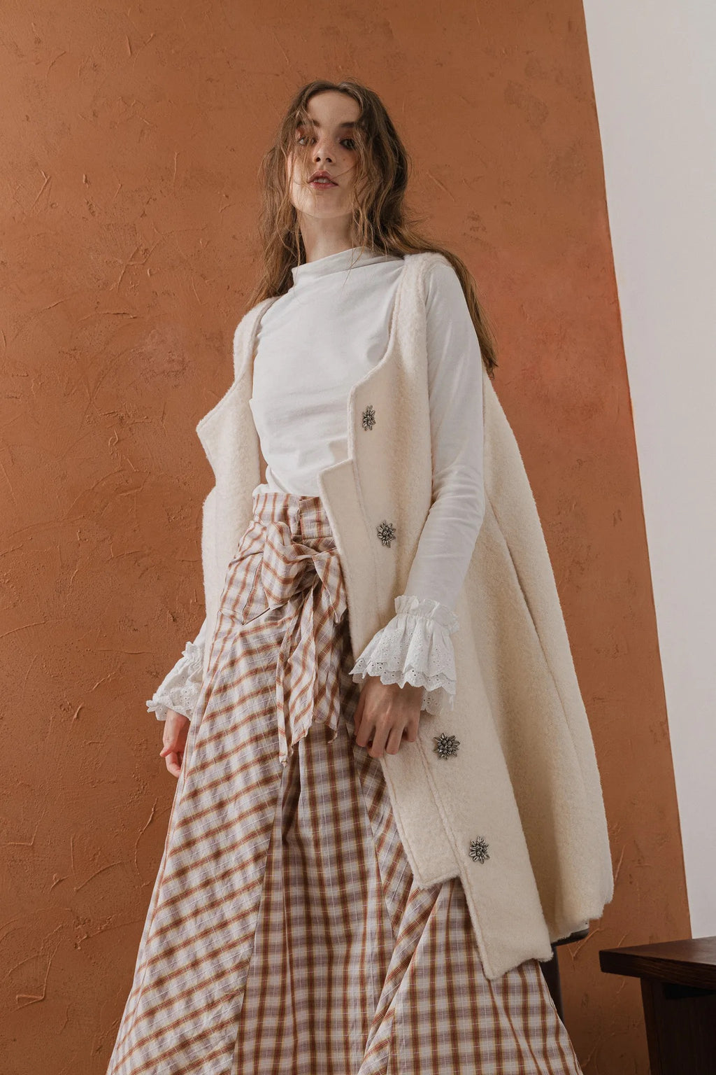 模特兒穿著燕麥白羊絨背心洋裝外套，柔軟羊絨面料搭配立體花釦、後開衩與側袋設計，展現優雅多變造型。