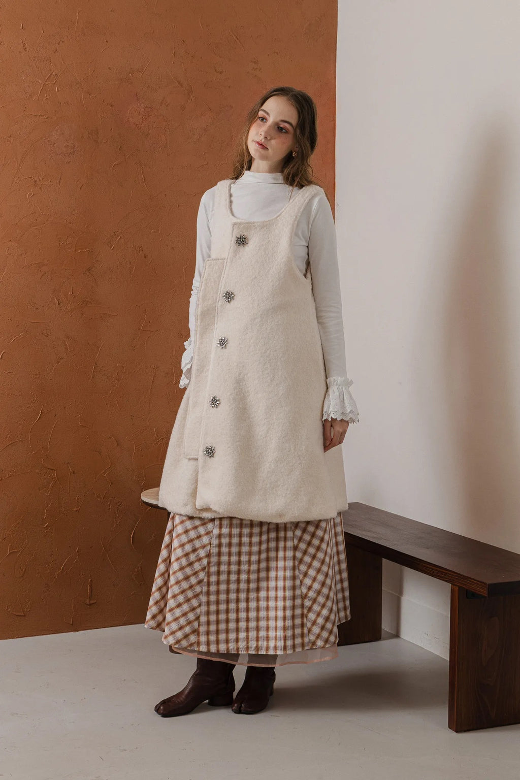 模特兒穿著燕麥白羊絨背心洋裝外套，柔軟羊絨面料搭配立體花釦、後開衩與側袋設計，展現優雅多變造型。