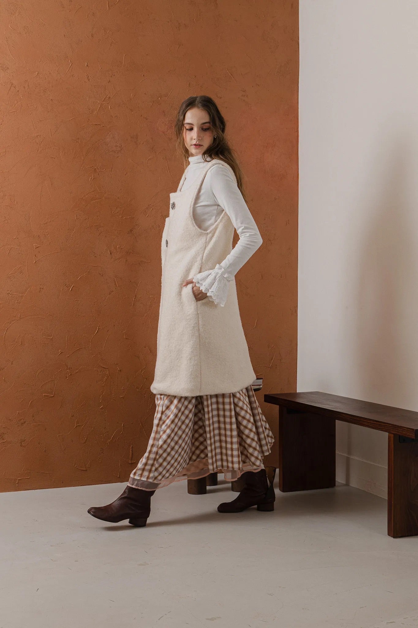 模特兒穿著燕麥白羊絨背心洋裝外套，柔軟羊絨面料搭配立體花釦、後開衩與側袋設計，展現優雅多變造型。