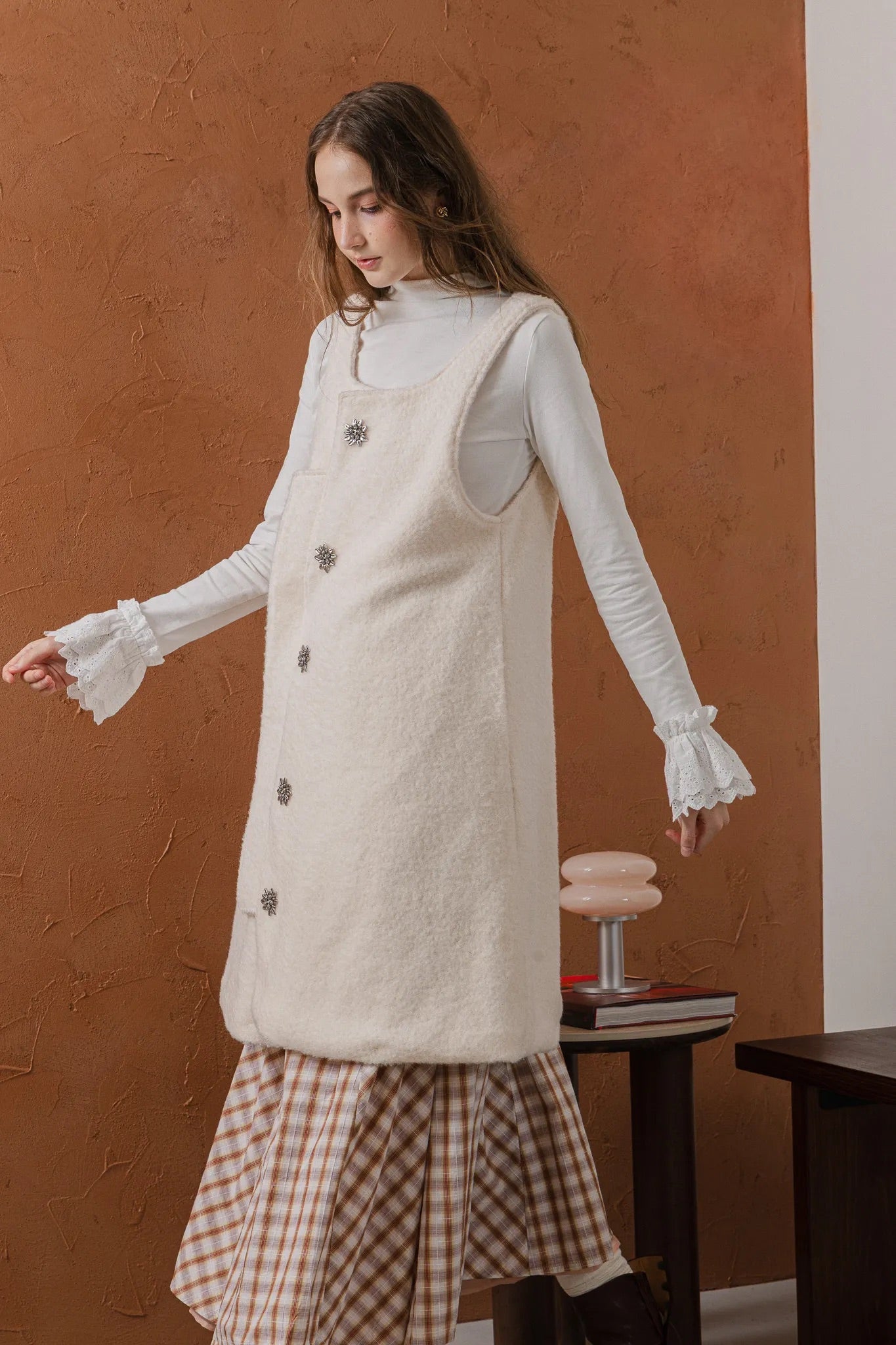 模特兒穿著燕麥白羊絨背心洋裝外套，柔軟羊絨面料搭配立體花釦、後開衩與側袋設計，展現優雅多變造型。