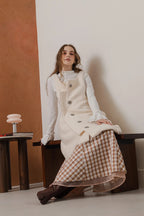 模特兒穿著燕麥白羊絨背心洋裝外套，柔軟羊絨面料搭配立體花釦、後開衩與側袋設計，展現優雅多變造型。