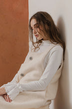 模特兒穿著燕麥白羊絨背心洋裝外套，柔軟羊絨面料搭配立體花釦、後開衩與側袋設計，展現優雅多變造型。