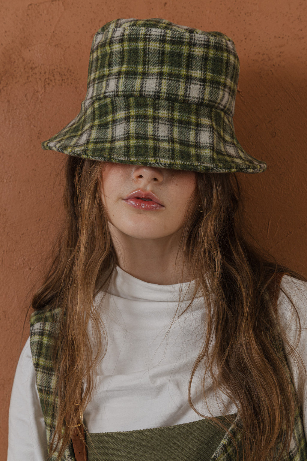 模特兒配戴手作羊毛格紋鐘形帽，綠白格紋面料與硬挺帽緣，呈現溫潤質感與修飾臉型的秋冬造型。