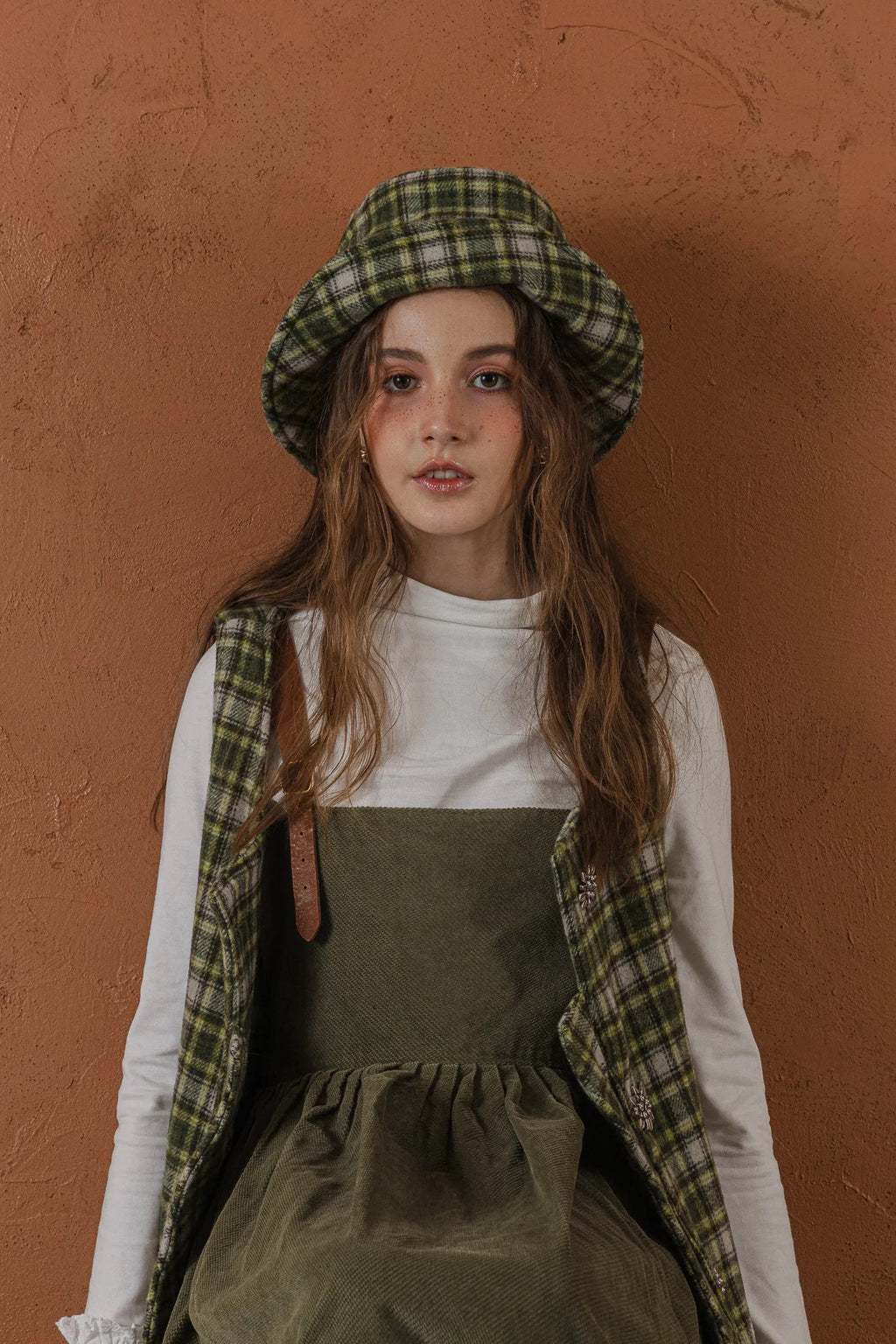 模特兒配戴手作羊毛格紋鐘形帽，綠白格紋面料與硬挺帽緣，呈現溫潤質感與修飾臉型的秋冬造型。