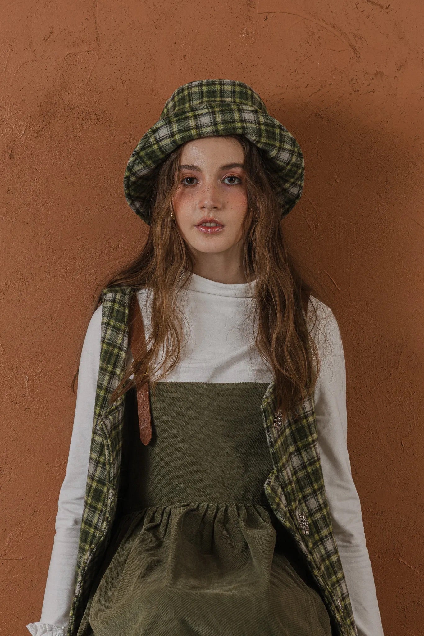 模特兒配戴手作羊毛格紋鐘形帽，綠白格紋面料與硬挺帽緣，呈現溫潤質感與修飾臉型的秋冬造型。
