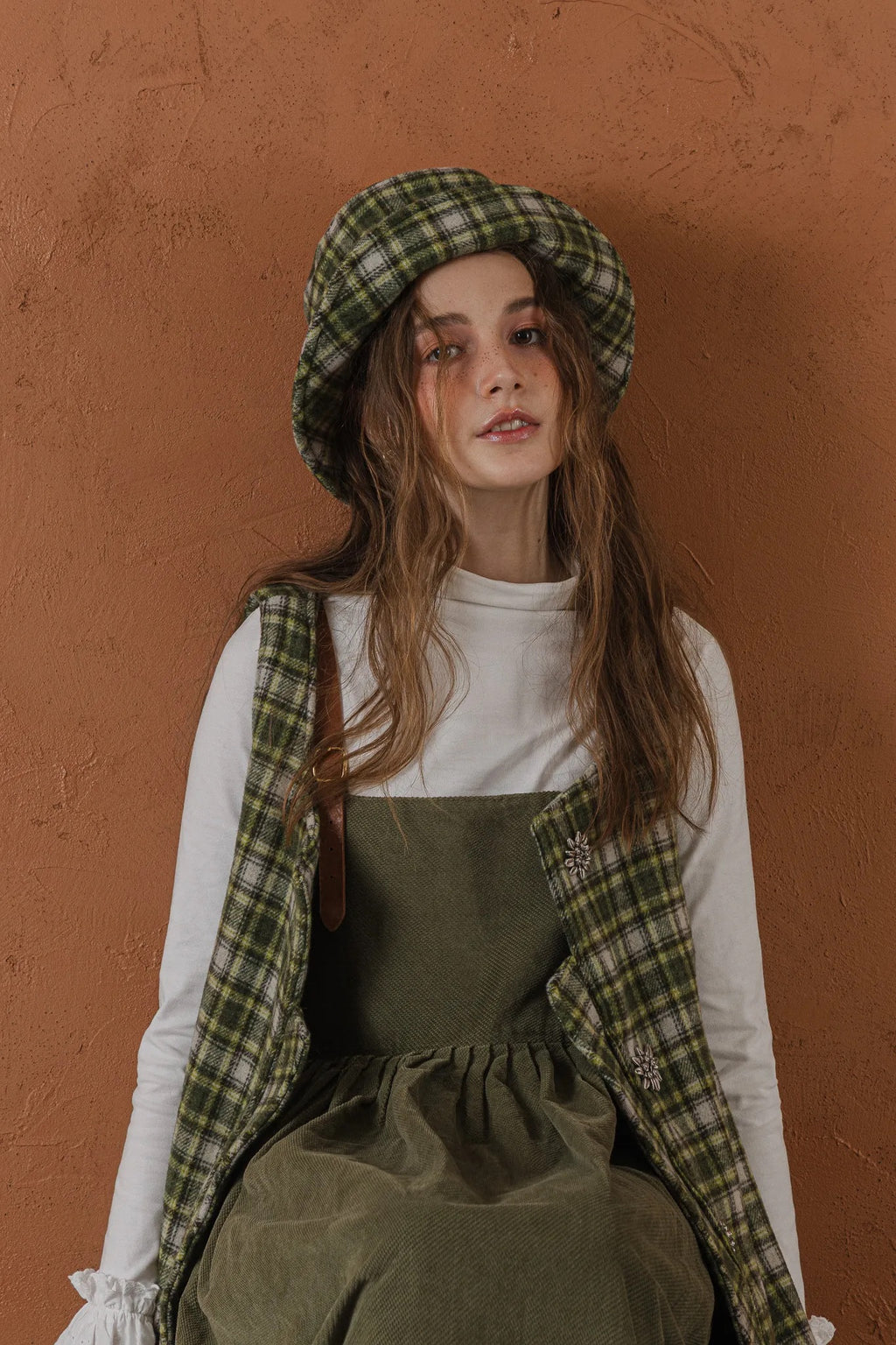 模特兒配戴手作羊毛格紋鐘形帽，綠白格紋面料與硬挺帽緣，呈現溫潤質感與修飾臉型的秋冬造型。