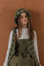 模特兒配戴手作羊毛格紋鐘形帽，綠白格紋面料與硬挺帽緣，呈現溫潤質感與修飾臉型的秋冬造型。