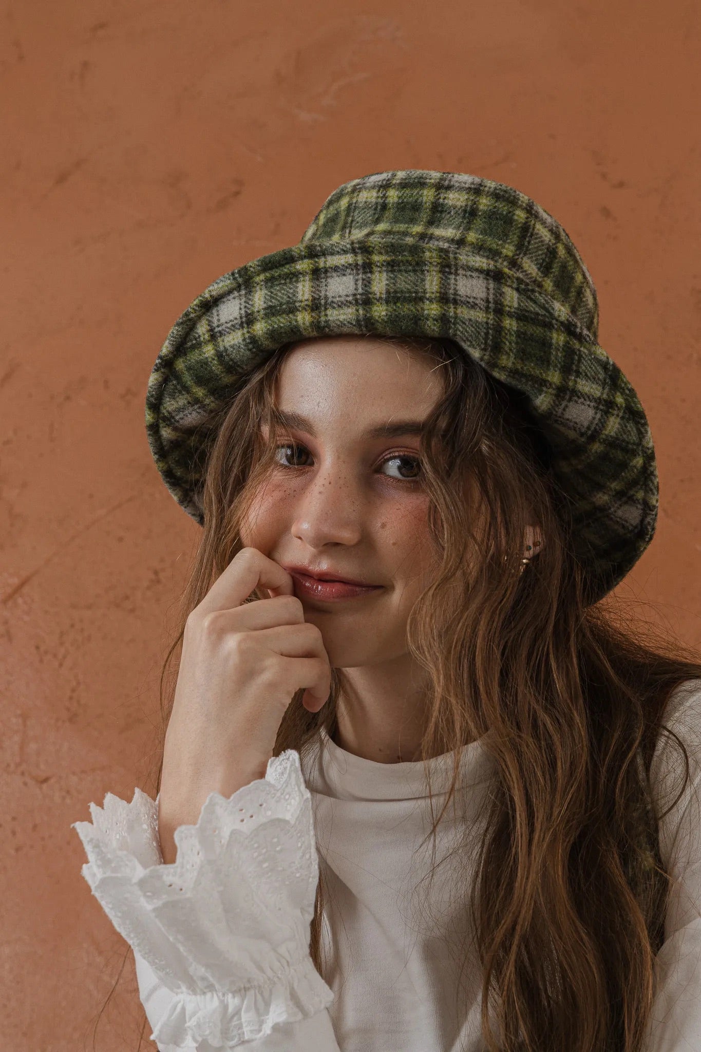 模特兒配戴手作羊毛格紋鐘形帽，綠白格紋面料與硬挺帽緣，呈現溫潤質感與修飾臉型的秋冬造型。