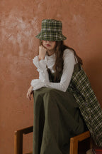 模特兒配戴手作羊毛格紋鐘形帽，綠白格紋面料與硬挺帽緣，呈現溫潤質感與修飾臉型的秋冬造型。
