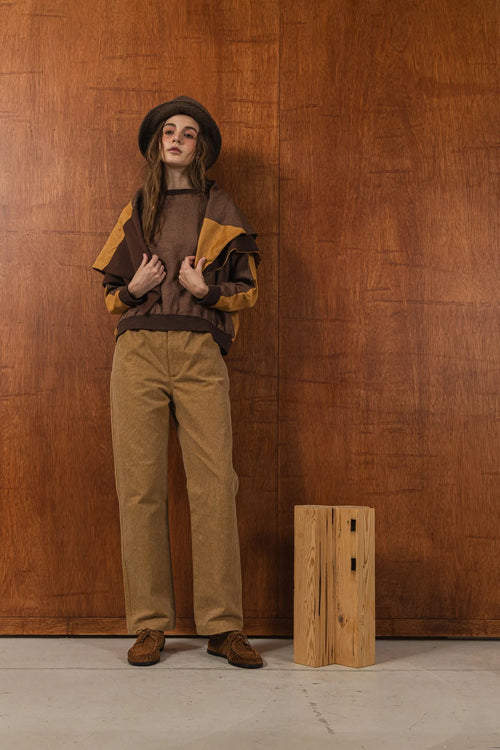 模特兒穿著拼接上衣披肩款，衣服為橘色與棕色拼接、多層次造型，呈現溫暖且有設計感的穿搭風格。