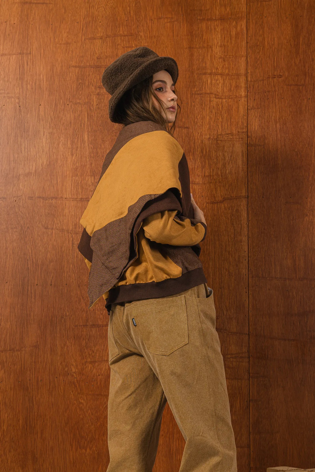 模特兒穿著拼接上衣披肩款，衣服為橘色與棕色拼接、多層次造型，呈現溫暖且有設計感的穿搭風格。