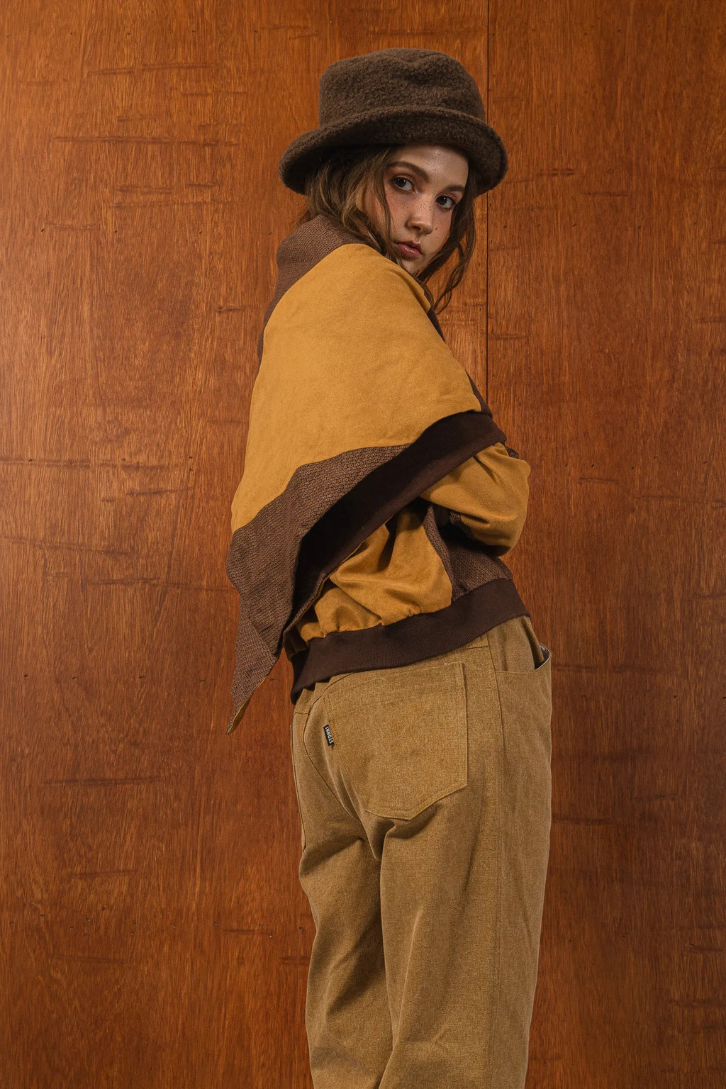 模特兒穿著拼接上衣披肩款，衣服為橘色與棕色拼接、多層次造型，呈現溫暖且有設計感的穿搭風格。