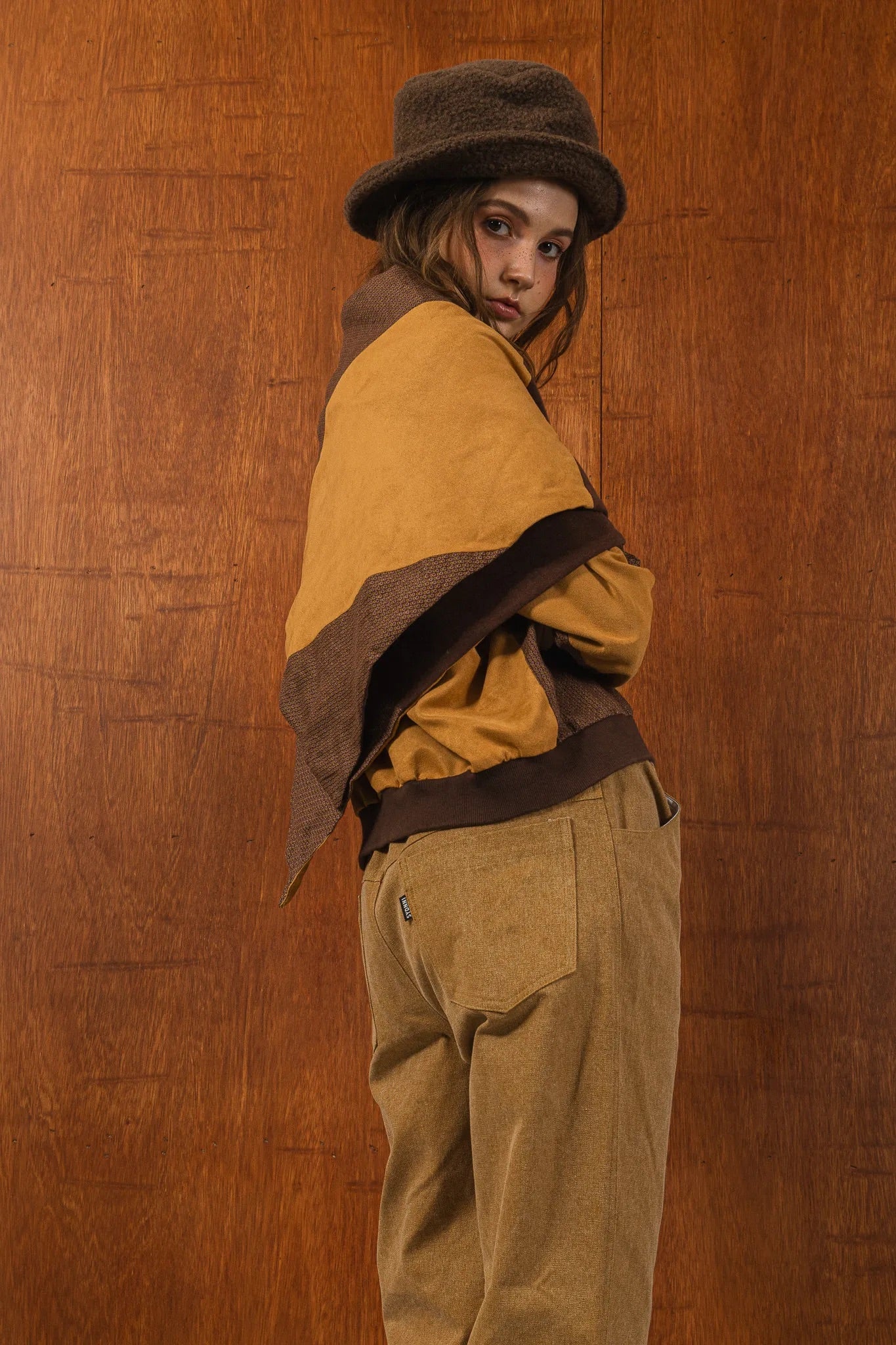 模特兒穿著拼接上衣披肩款，衣服為橘色與棕色拼接、多層次造型，呈現溫暖且有設計感的穿搭風格。