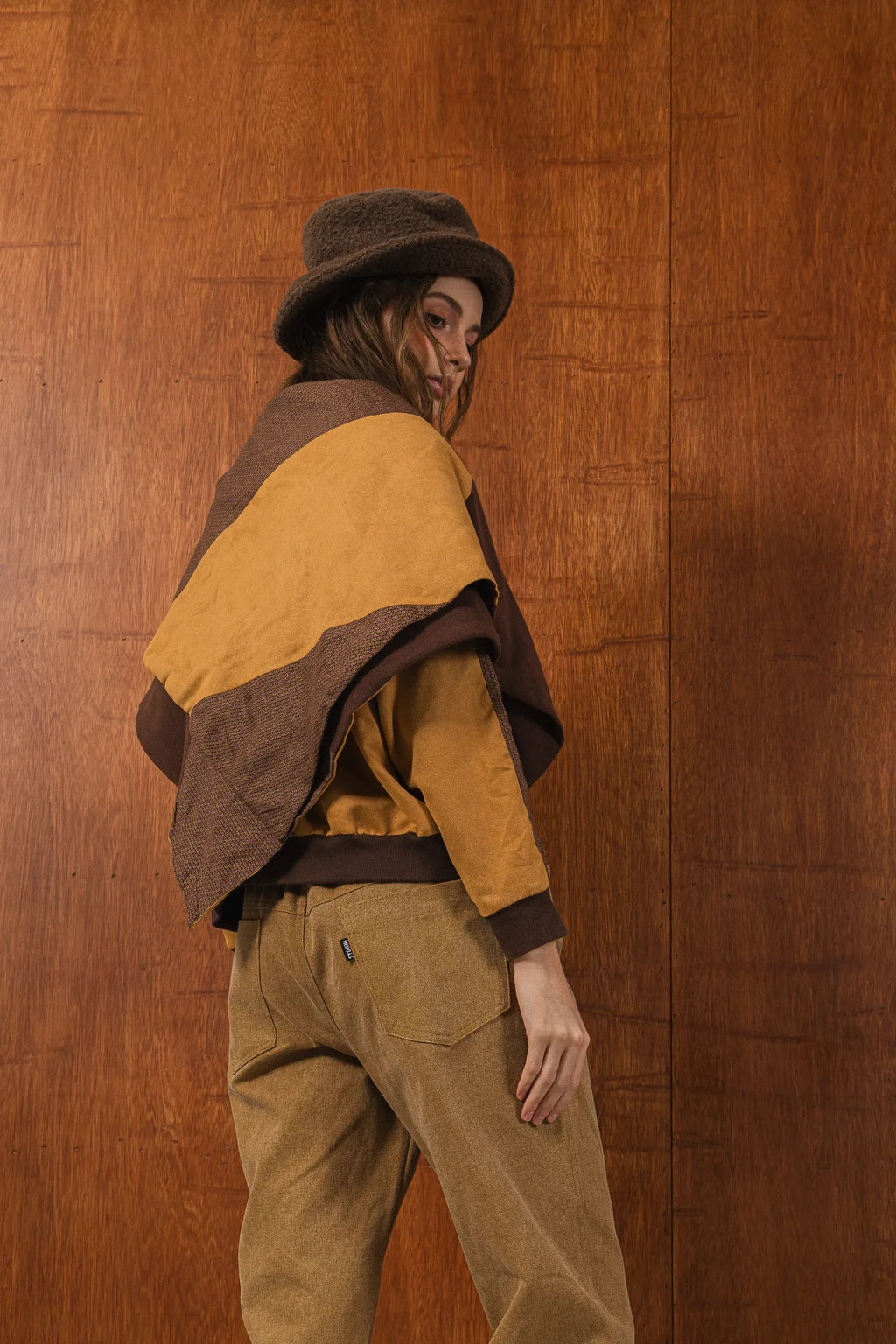 模特兒穿著拼接上衣披肩款，衣服為橘色與棕色拼接、多層次造型，呈現溫暖且有設計感的穿搭風格。