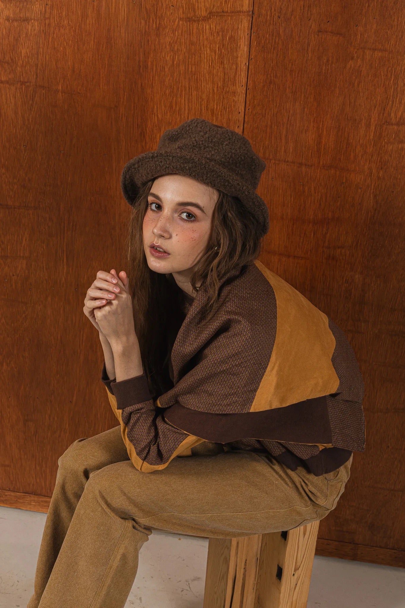 模特兒穿著拼接上衣披肩款，衣服為橘色與棕色拼接、多層次造型，呈現溫暖且有設計感的穿搭風格。