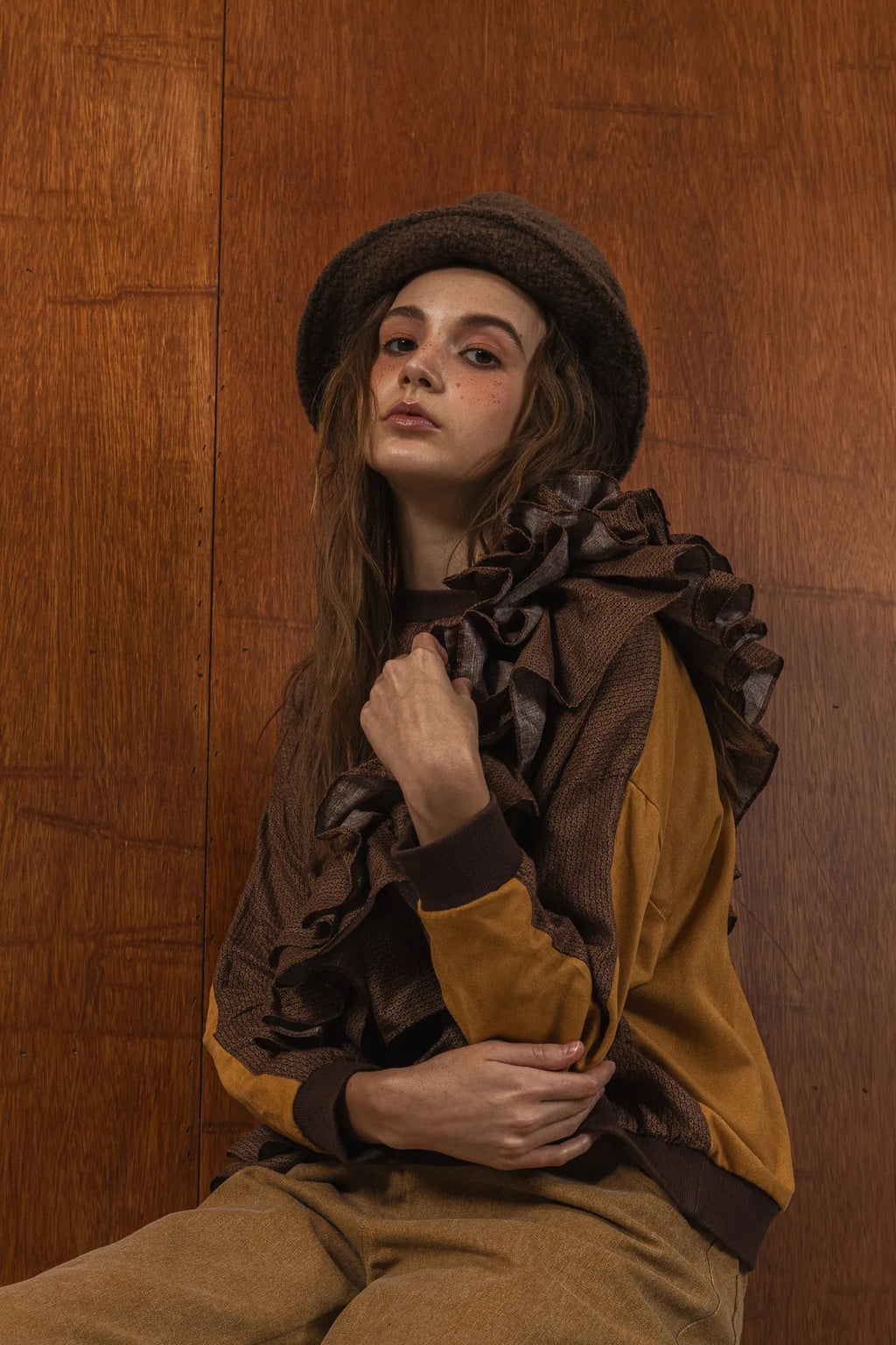 模特兒穿著拼接上衣Puff荷葉款，衣服為橘色與棕色拼接、華麗造型，呈現溫暖且有設計感的穿搭風格。