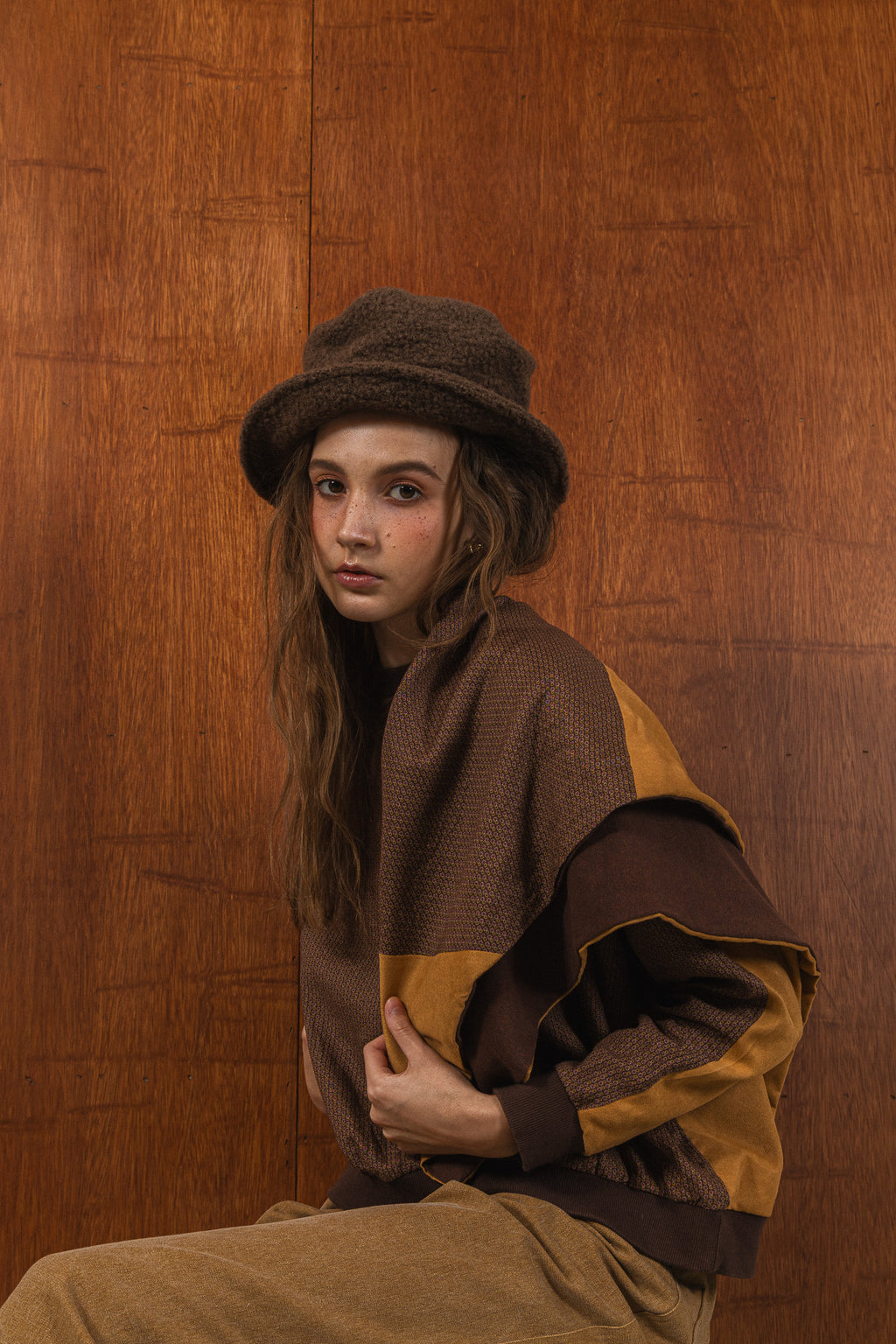 模特兒穿著拼接上衣披肩款，衣服為橘色與棕色拼接、多層次造型，呈現溫暖且有設計感的穿搭風格。