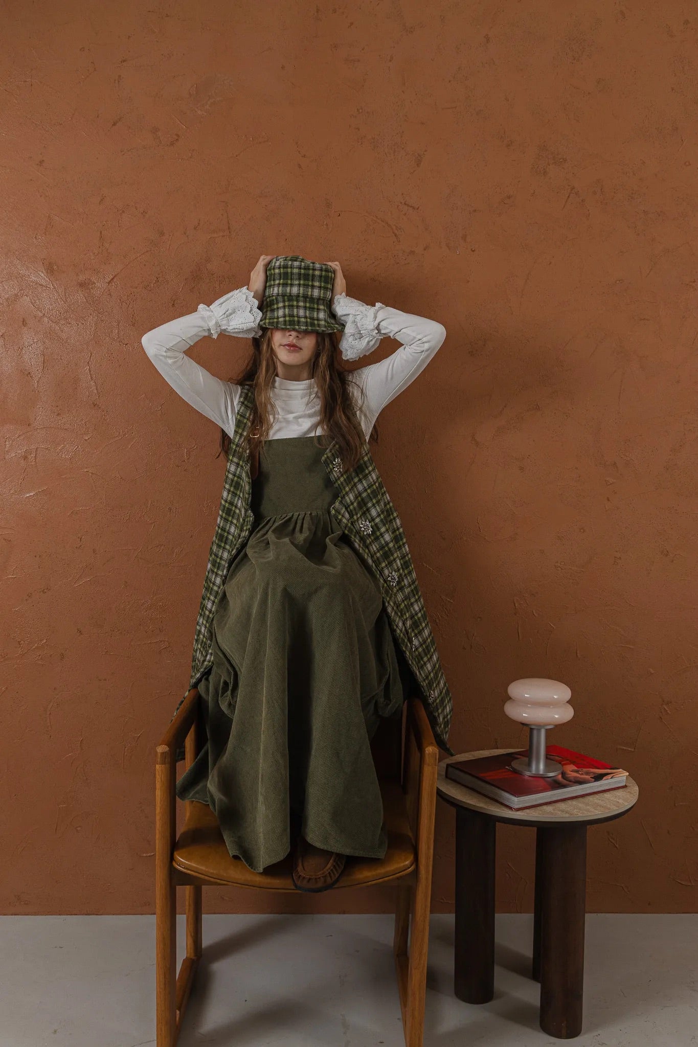 模特兒穿著羊毛格紋背心洋裝外套，經典學院風格紋搭配獨特門襟與手縫立體花釦，後開衩與側口袋設計呈現優雅又隨性的造型。