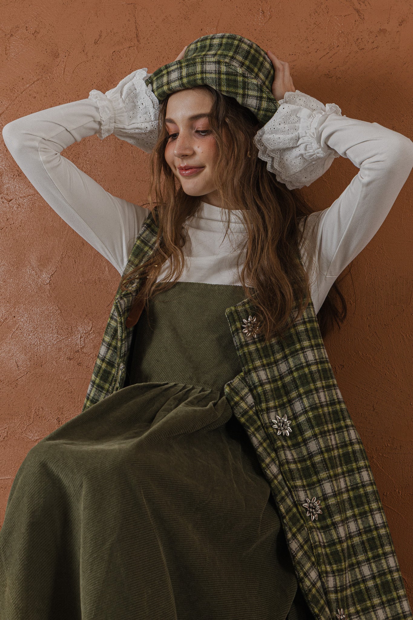 模特兒穿著羊毛格紋背心洋裝外套，經典學院風格紋搭配獨特門襟與手縫立體花釦，後開衩與側口袋設計呈現優雅又隨性的造型。